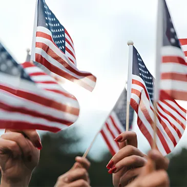 A group of hands holding small American flags against a soft-focus background, celebrating patriotism.
